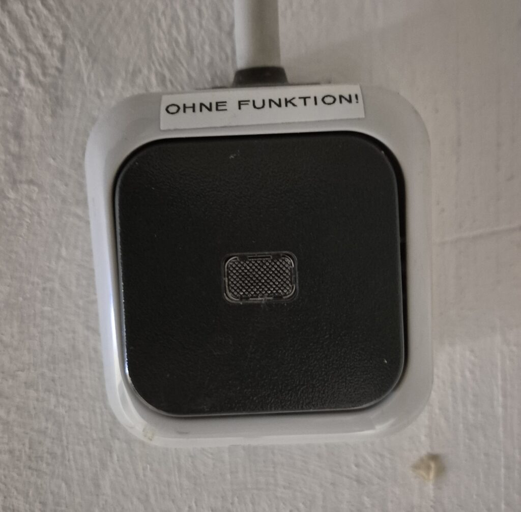 Foto eines Lichtschalters auf dreckigem Putz, auf dem ein Aufkleber mit der Aufschrift "Ohne Funktion!" angebracht ist.